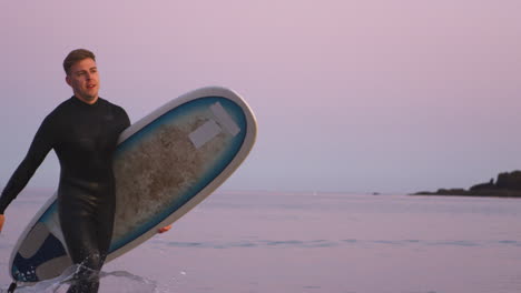 hombre con traje de buceo llevando una tabla de surf mientras sale del mar