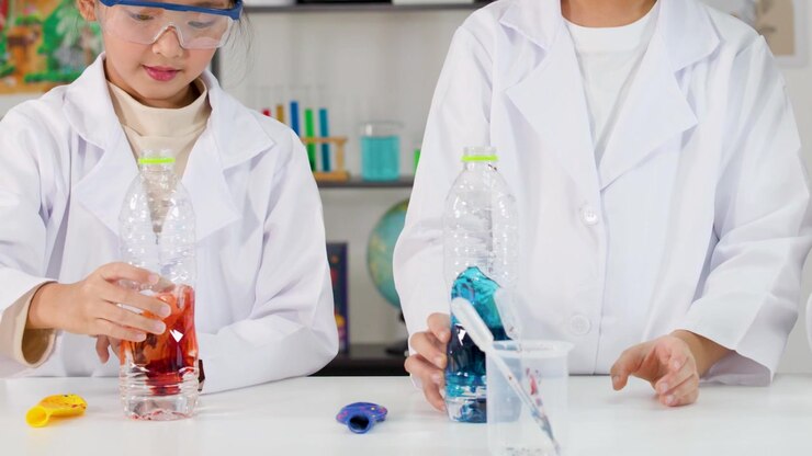 Asiatiske studerende i laboratoriekittel bruger pipetter til at blande farvede væsker under et videnskabeligt eksperiment