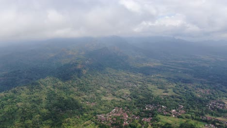 Wolken-über-Bergen-Und-Einer-Kleinstadt-Unten-In-Indonesien,-Drohnenansicht-Aus-Der-Luft