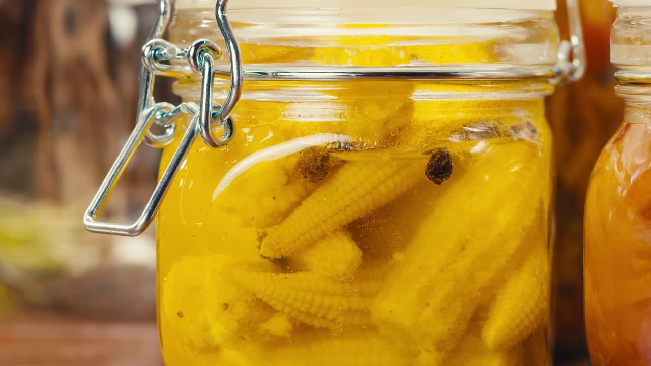 Close-up of fermented yellow mini corn with black pepper in can. Preservation of vegetables in glass jars. Fermentation preserved mini corns with spices.
