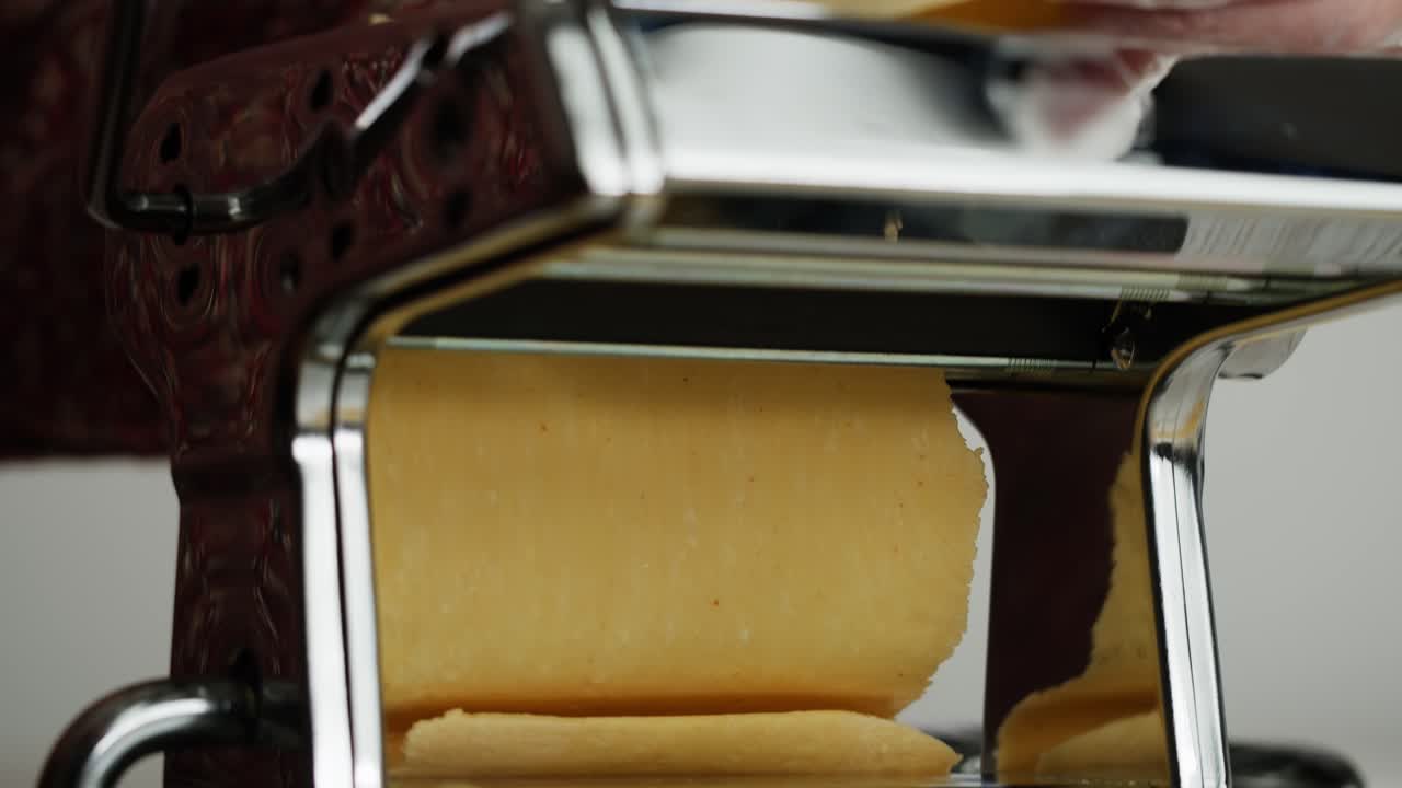 Close-up of Hands Rolling Fresh Pasta Dough Through a Machine