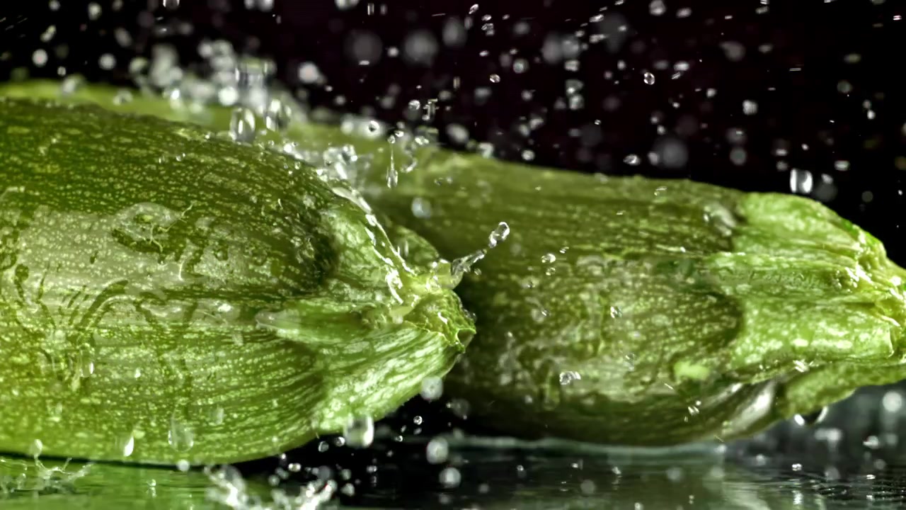 Gocce d'acqua che schizzano su zucchine verdi fresche al rallentatore.