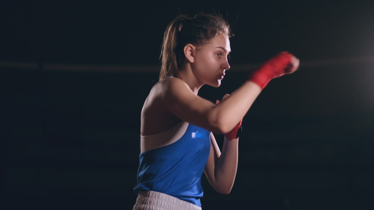 Beautiful woman fighter in red bandages conducts a shadow fight while exercising in the gym. Slow motion. steadicam shot