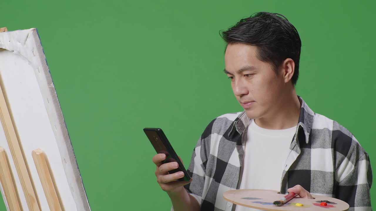 페인팅 용품 근처 에 있는 전화 를 보고 있는 예술가