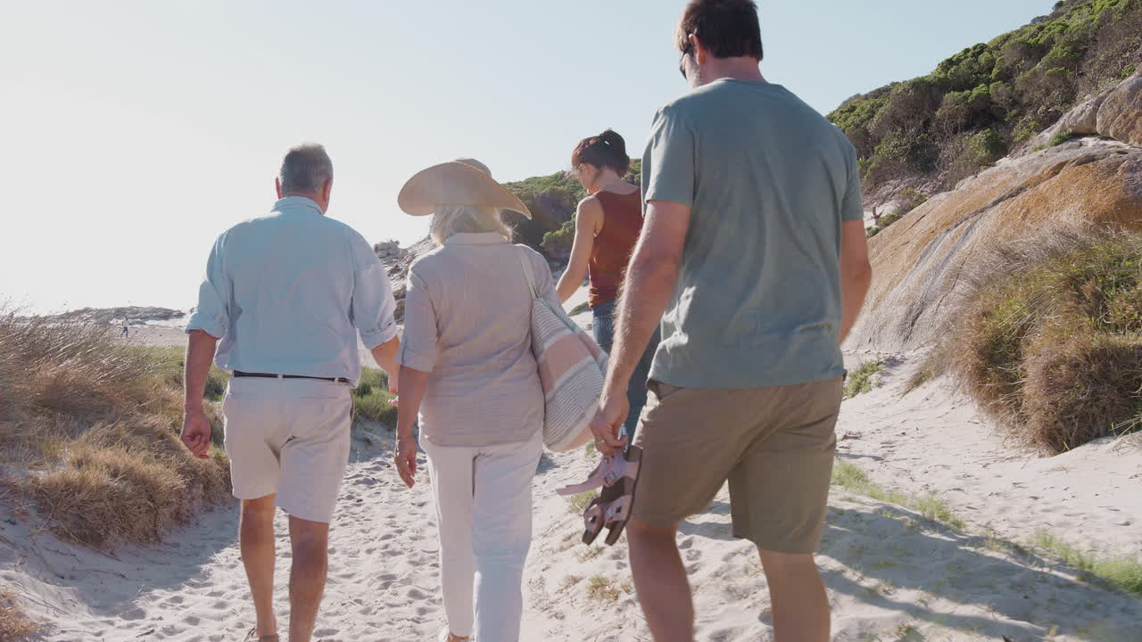 familia de varias generaciones en vacaciones de verano caminando por un camino de arena de camino a la playa