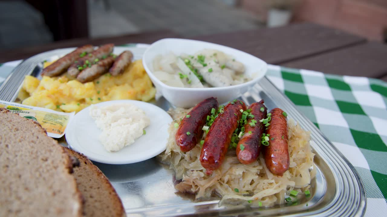 Hand uses fork to take sausage from plate with sauerkraut, potato salad, bread, horseradish