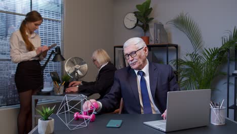 Hombre-De-Negocios-Haciendo-Ejercicios-Con-Pesas-De-Fitness-Después-De-Un-Duro-Trabajo-Mientras-Se-Sienta-En-El-Escritorio-De-La-Oficina