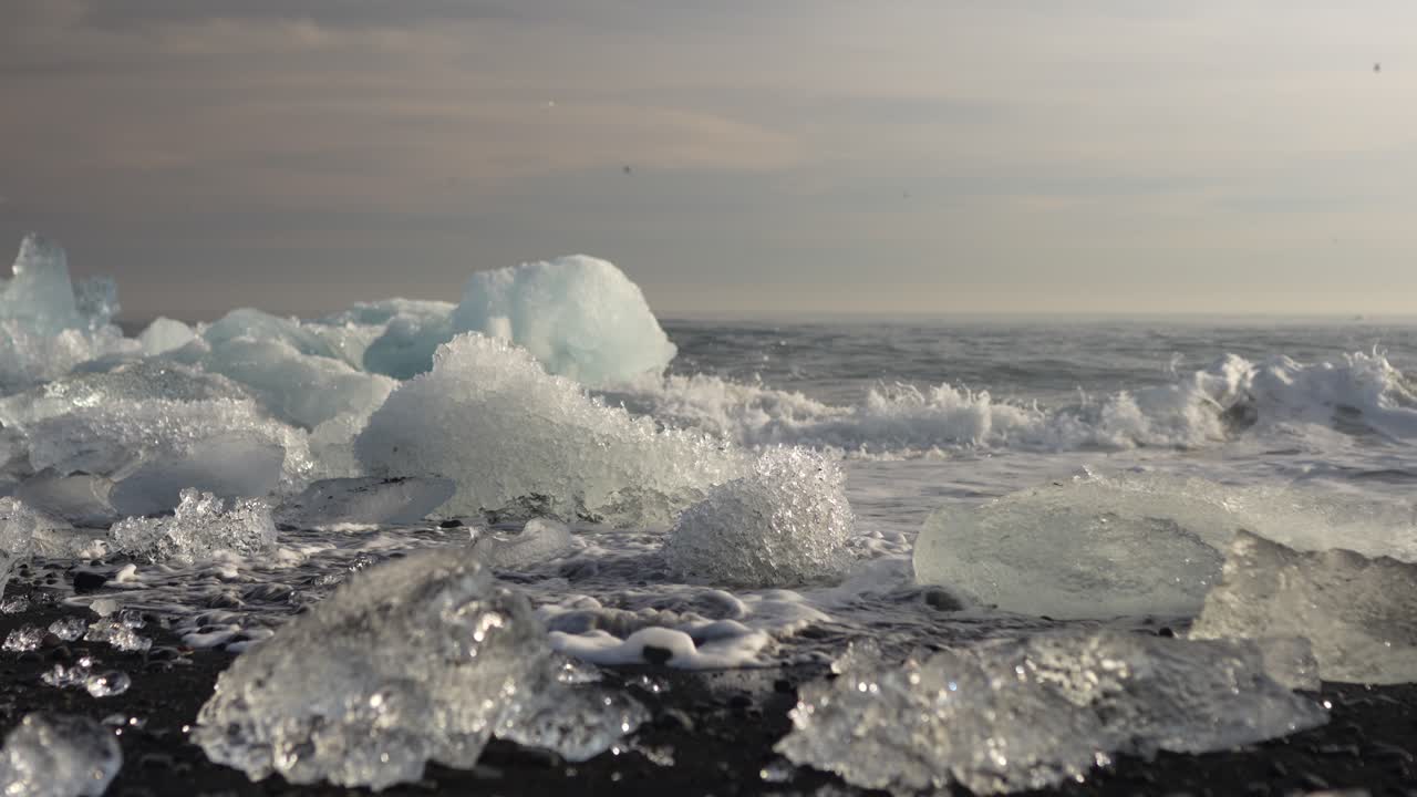 Glittering ice chunks on the black sand of Diamond Beach by the North Atlantic Ocean in Iceland