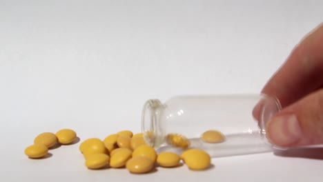 las pastillas amarillas salen de una botella de vidrio.