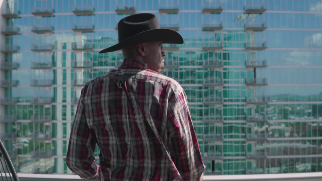 Uomo di colore con cappello da cowboy nero che guarda da un balcone.