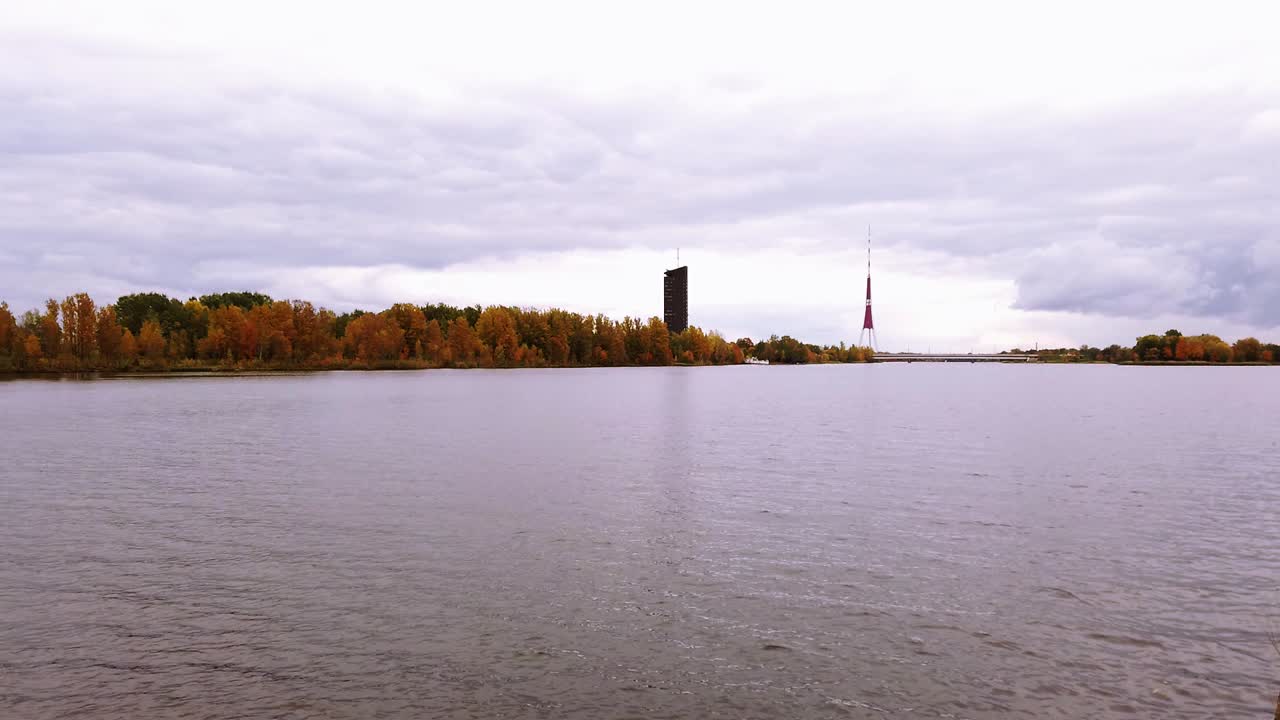 телевизионная башня риги с берега реки даугува с тихой и спокойной водой в пасмурный осенний день