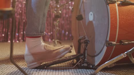 a close-up, low-angle shot of a drummer's foot in a stylish loafer, rhythmically playing the bass drum pedal. the vintage drum and sparkly background suggest a live music performance or band practice.