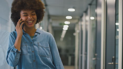 smiling businesswoman standing in corridor of modern office talking on mobile phone