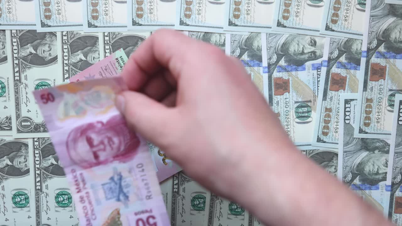 una persona que pone varios billetes mexicanos encima de los billetes estadounidenses. concepto: tasas de cambio del peso mexicano
