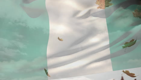 digital composition of nigeria waving flag over autumn leaves falling against clouds in the sky