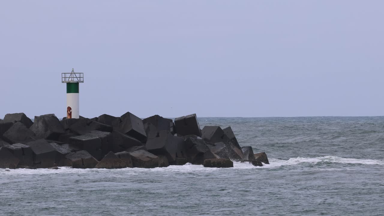 las olas del océano golpean las rocas cerca de un faro verde