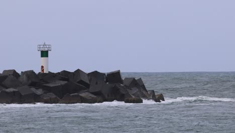 ocean waves hitting rocks near a green beacon