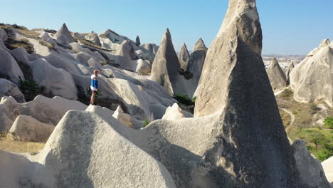 epic revealing cinematic drone shot of a lone man standing among the fairy chimneys and revealing a large city in cappadocia, turkey