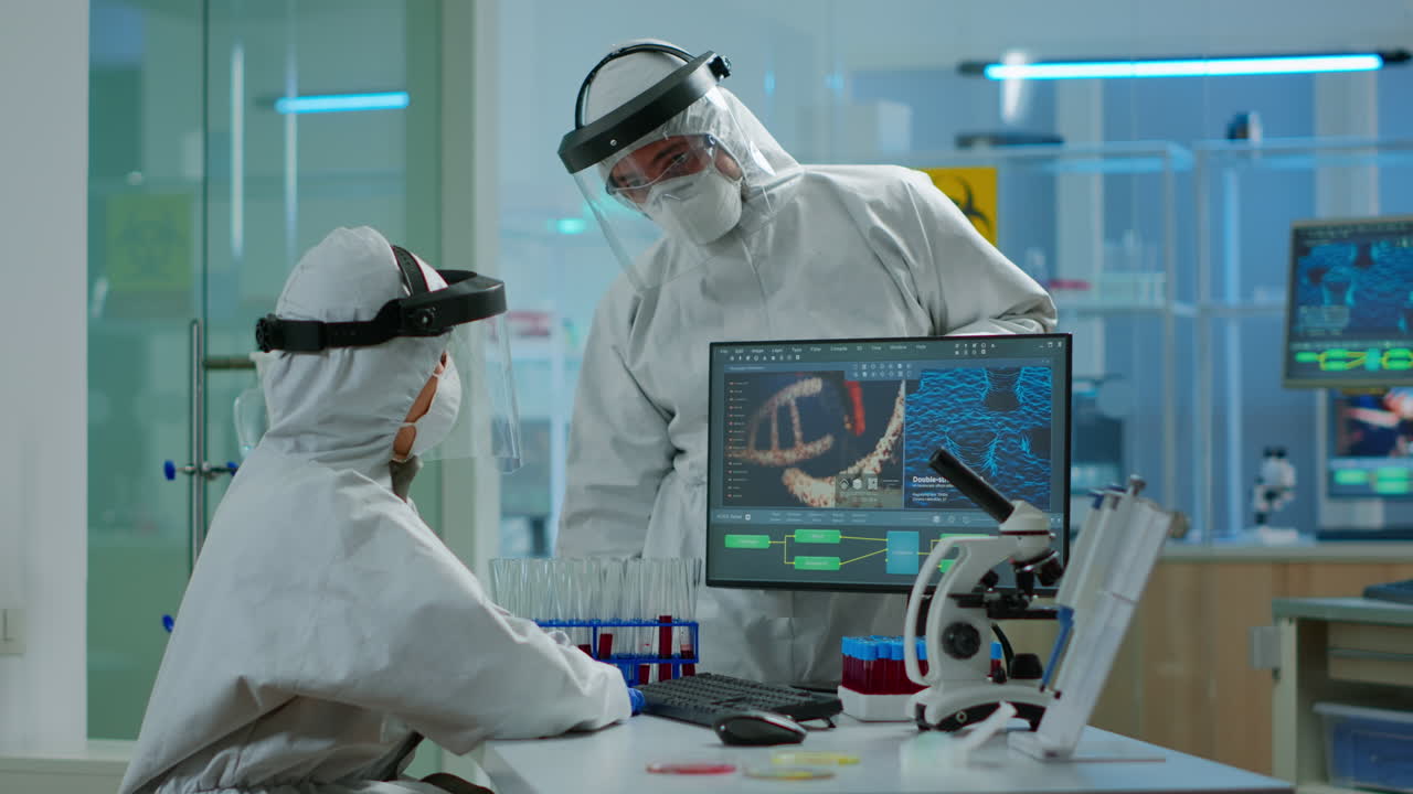 프로렉션 슈트를 입은 과학자 팀이 pc 앞에서 바이러스 개발을 보고 논쟁하고 있습니다.