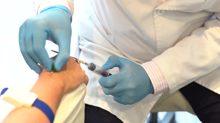 Woman's hand with needle inside has blood drawn by a male doctor.