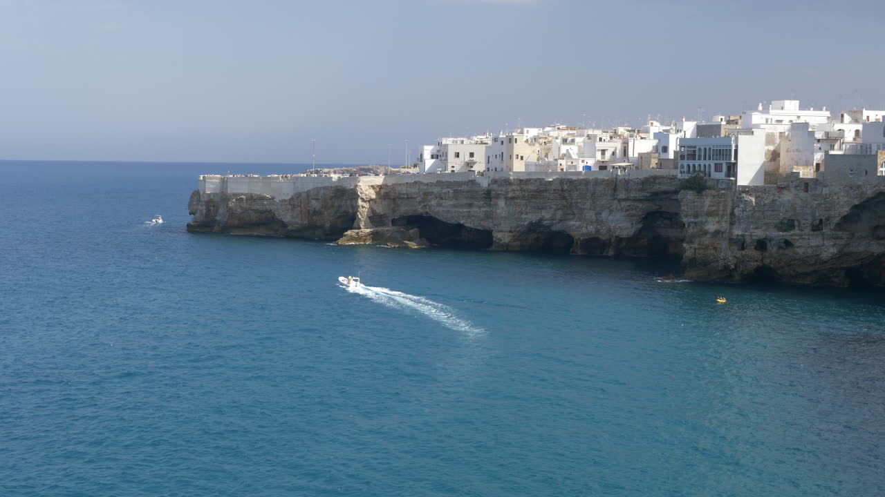 Una barca che naviga al rallenty attraverso il Mare Adriatico con vista su edifici sulla scogliera a Polignano a Mare, Italia