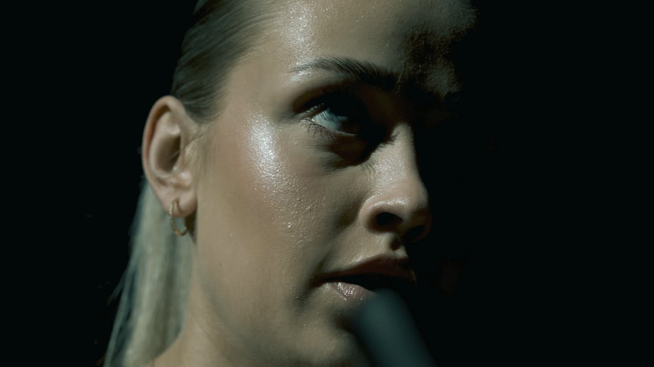 Intense closeup of a woman’s face mid-training, captured from a low angle through the bike’s handlebars. Sweat, focus, and cinematic light highlight her strength and concentration in a tight frame