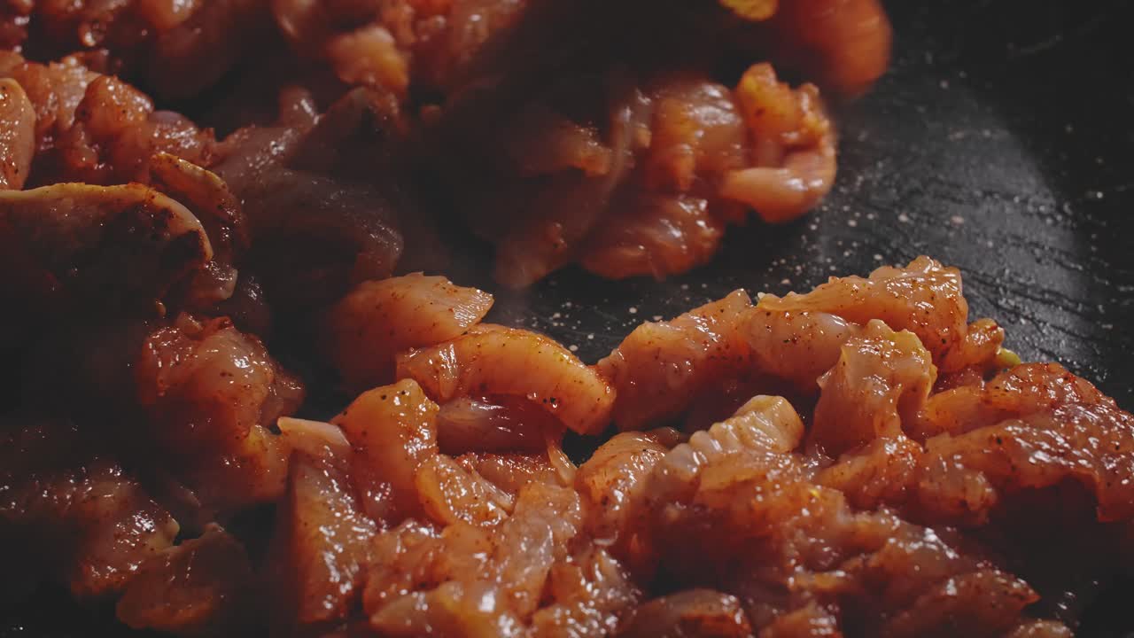 un primer plano de trozos de pechuga de pollo humeantes cortados y sazonados en una sartén caliente y luego revueltos con una cuchara de madera, extendiéndolos uniformemente