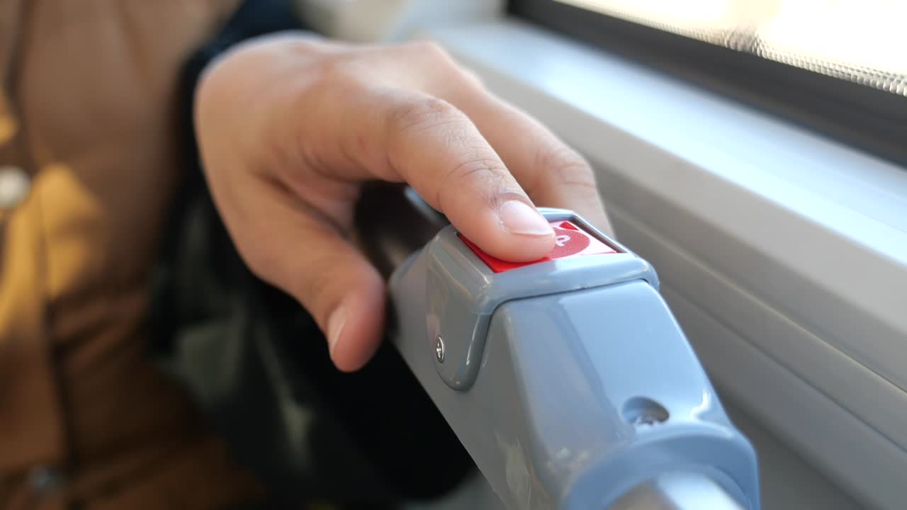 A hand pressing a stop button on a bus
