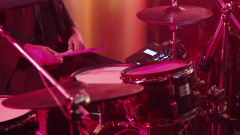 drummer playing a drum kit under vibrant red and orange lighting during a live performance