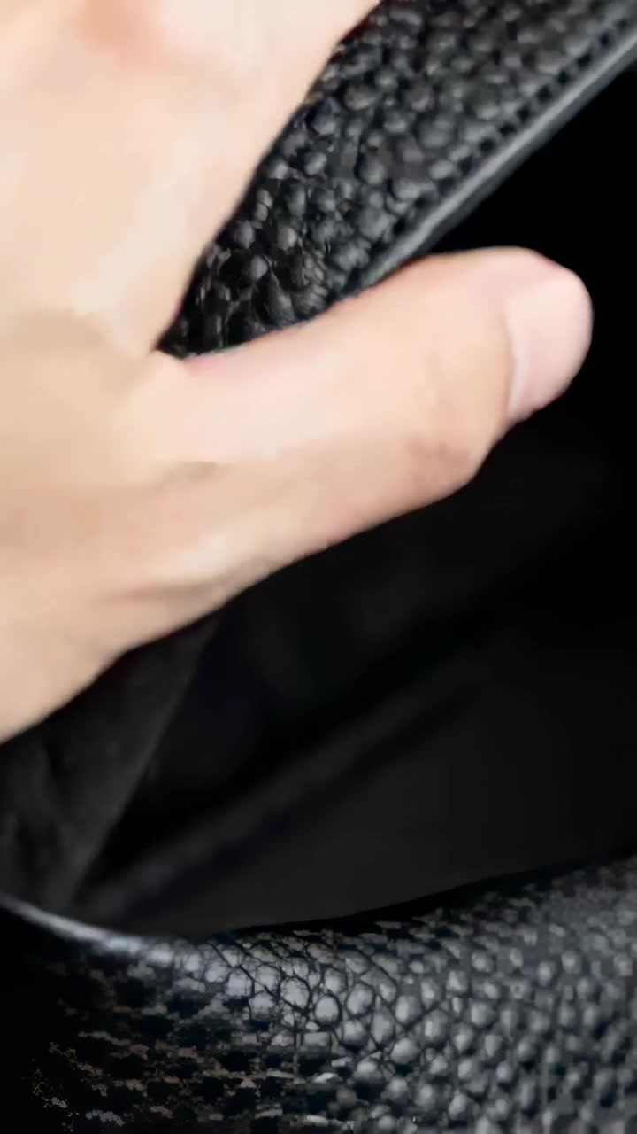 Video vertical: Mano agarrando y tirando de una correa de cuero negro granulado en primer plano, examinando el forro.