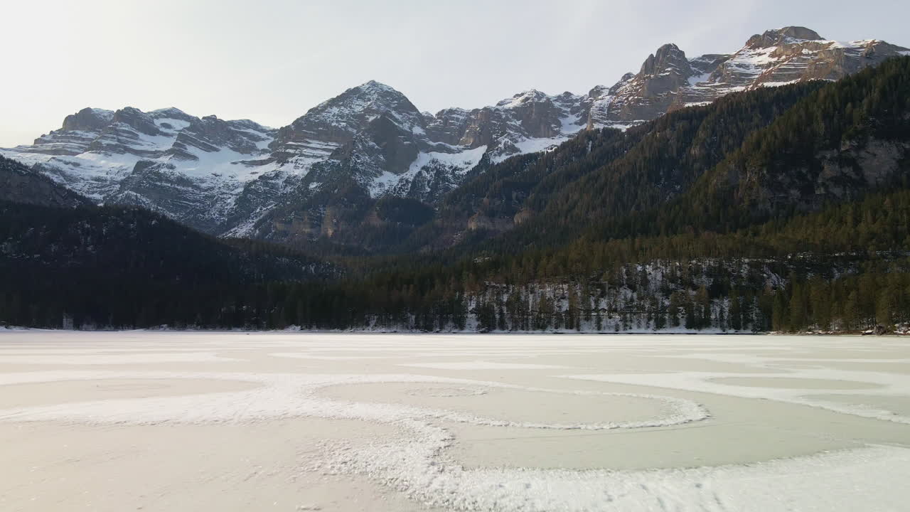 Elokuvallinen lento jäätyneen Tovel-järven yllä, jota ympäröi tiheä metsä kylmänä talviaamuna Trentinossa, Italiassa.