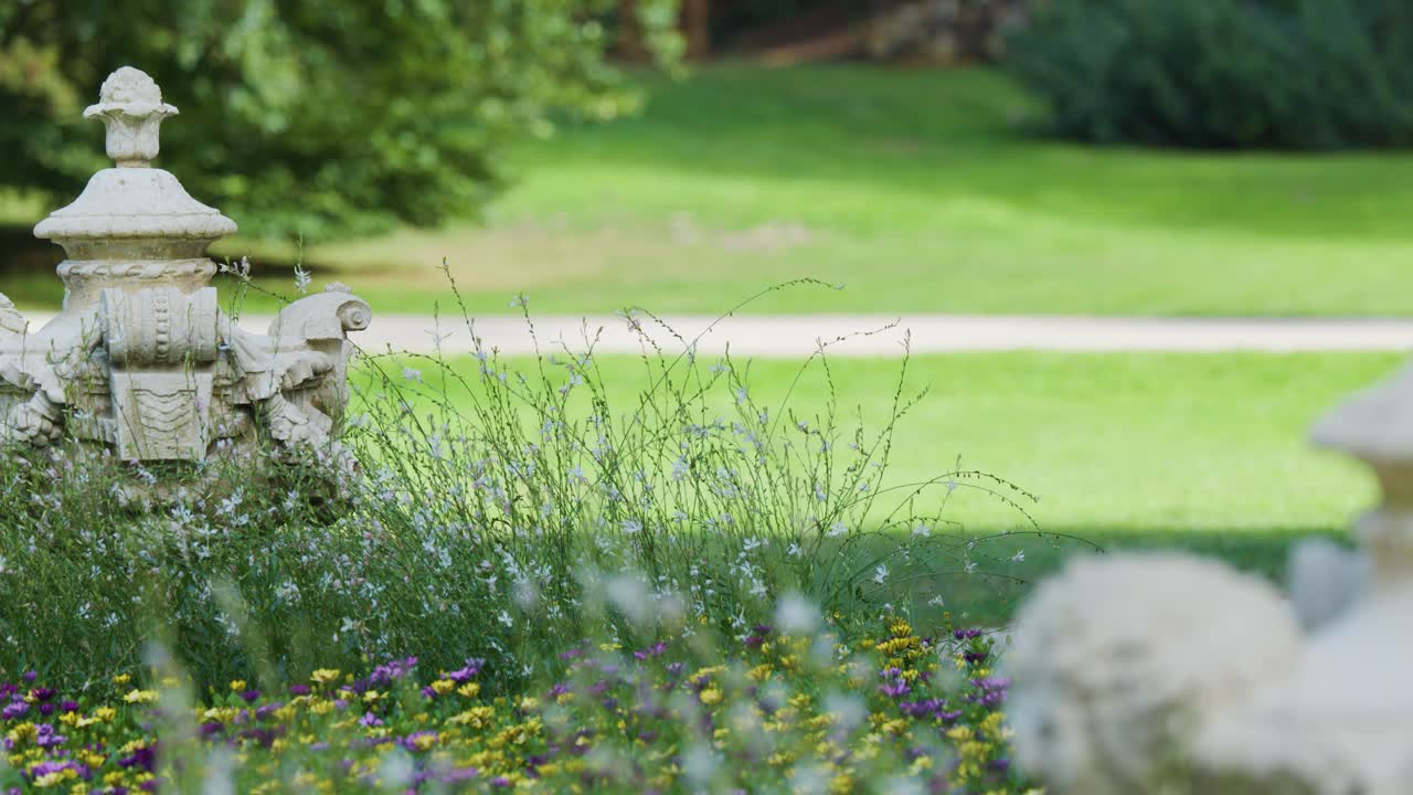 Two sparrows rest on a stone lantern amid flowers, soft daylight, shallow focus, static shot