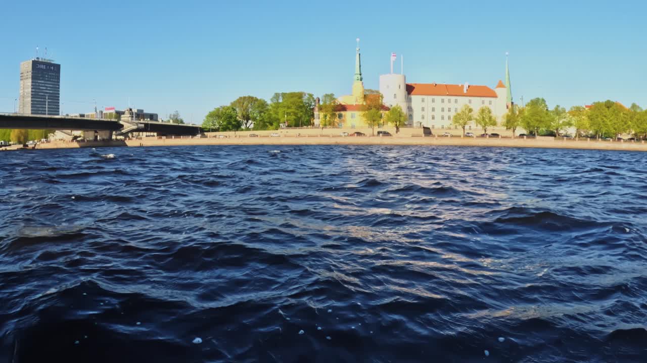 Panoramic view of Riga’s riverfront with historic towers, Riga castle and calm waves on a bright summer day, perfect for travel, tourism, European waterfront
