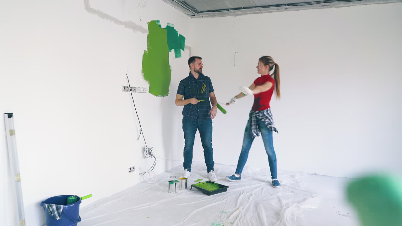pareja en vaqueros baila levantando herramientas de pintura abrazos en la habitación