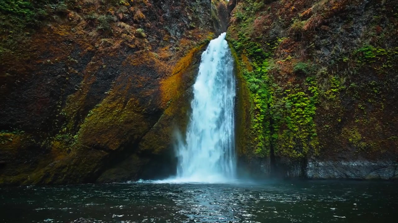 Handheld wide panning shot of the beautiful Wahkeena Waterfall cascading through narrow rocky canyon with moss and forestry.