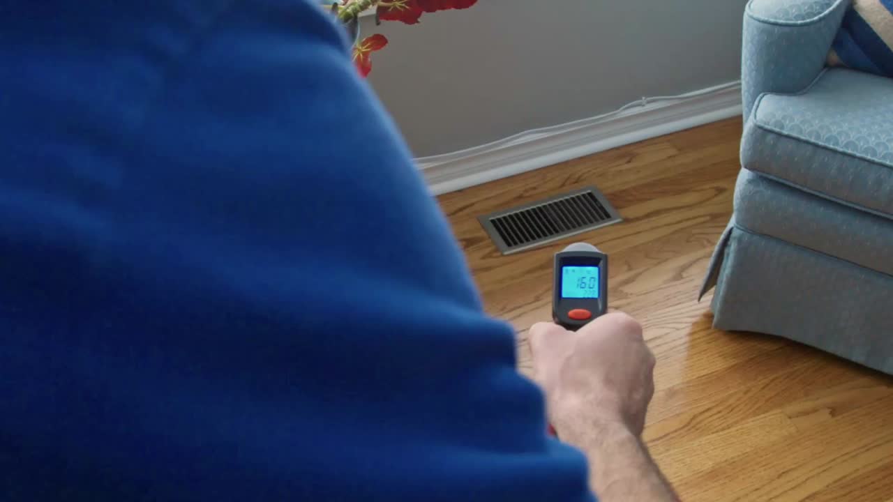 Home inspector uses a infra red thermometer to check the temperature coming out of floor register. Various temperatures are displayed