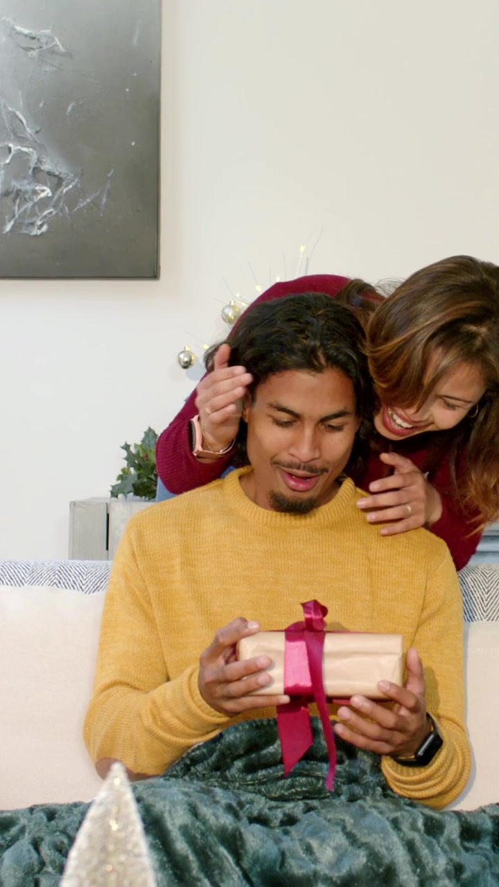 Video verticale: Donna in rosso che si avvicina furtivamente, si copre gli occhi, porge un regalo e lo guarda aprire la scatola per Natale.