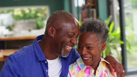 Portrait-Of-Smiling-Loving-Senior-Couple-Sitting-On-Sofa-At-Home-Together