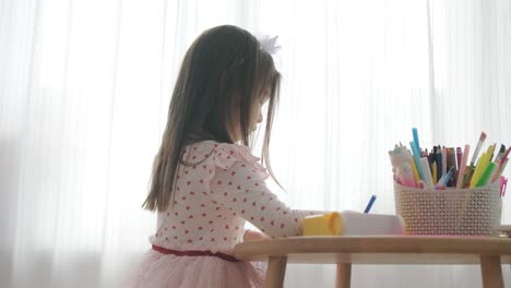 young girl sitting at a table, drawing with colorful crayons. ideal for themes of creativity, childhood development, learning, and art activities in a cozy indoor setting.