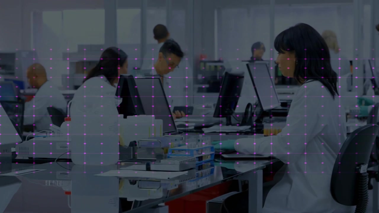 Seated lab tech typing at PC in clinical lab, magenta waveform appearing, staff checking monitors