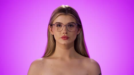 Medium-shot-of-an-attractive-young-woman-or-model-with-glasses-looking-seductively-at-the-camera-while-adjusting-her-glasses-on-her-face-in-front-of-purple-background-in-slow-motion