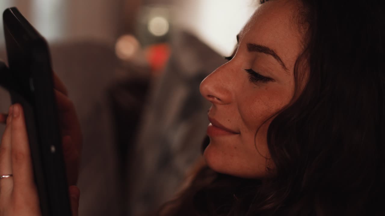 집에서 소파에 앉아 미소 짓는 이탈리아의 젊은 여성이 태블릿을 사용하고 있습니다.