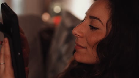 young italian woman using a tablet while sat on the sofa at home smiling
