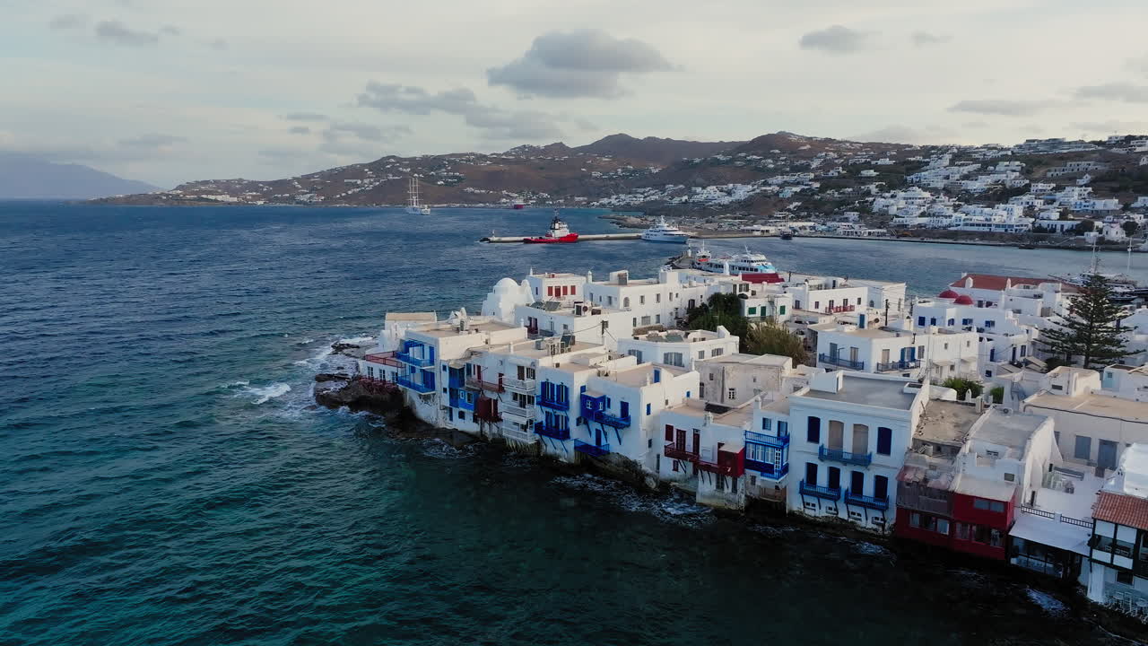 Piccola Venezia Mykonos con case bianche sulla costa rocciosa, barche nella baia dell'Egeo sotto la luce della sera.