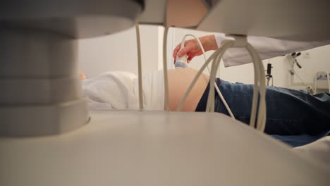 a woman is receiving an ultrasound in a hospital room with wood flooring and metal ceiling. the art on the walls depicts circles