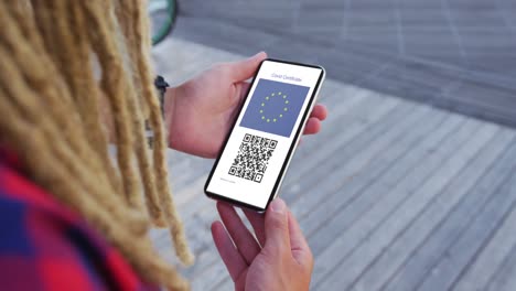 Man-with-dreadlocks-holding-smartphone,-covid-vaccination-certificate,-eu-flag-and-qr-code-on-screen