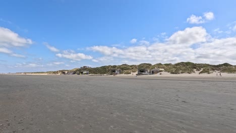 Static wide shot of a sandy beach and coastal dunes in Dunkirk, France, under bright daylight with scattered clouds and minimal human presence