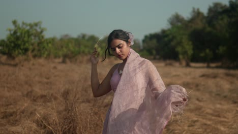 woman in pink dress with flowing veil in dry field, evokes feeling of freedom and elegance, sunny day