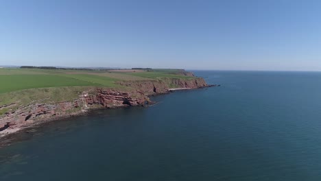 forward flying drone footage along cliffs at coastline with beautiful blue sky and blue sea.