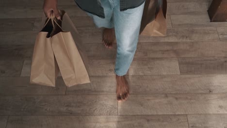 Man-is-walking-barefoot-over-the-wooden-floor-and-carrying-paper-bags-in-his-hands